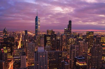 Illuminated cityscape against cloudy sky during dusk