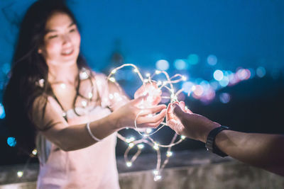 Close-up of couple holding illuminated lights against sky