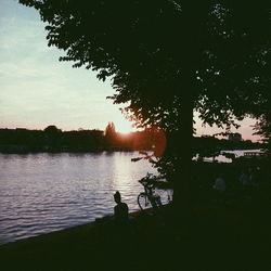 Silhouette man in lake against sky during sunset