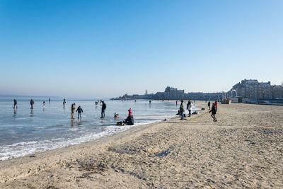 People on beach against clear blue sky