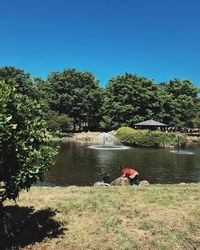 People sitting by lake against clear sky