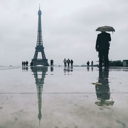 People standing on wet shore against sky