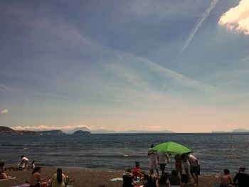 People relaxing at beach against sky during sunset