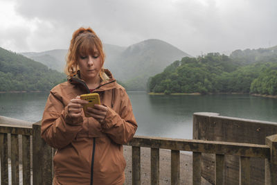 Caucasian woman using her smartphone  with a lake and mountains in the background on a cloudy day