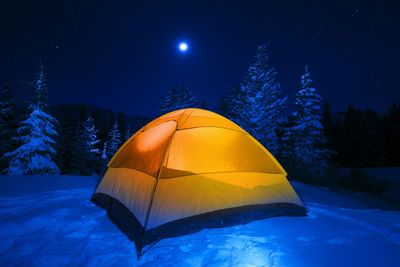 Illuminated tent on snowy landscape against sky at night