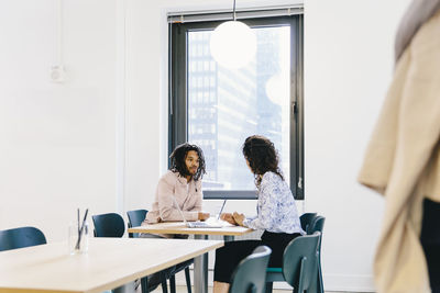 Businesswoman discussing with businessman while sitting at desk in office