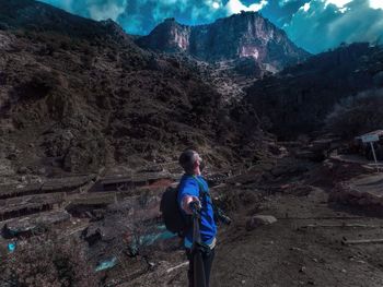 Side view of hiker standing on ground against mountains