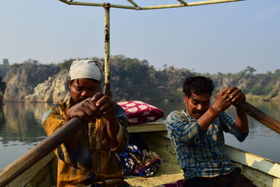 Men sitting on man holding umbrella against clear sky