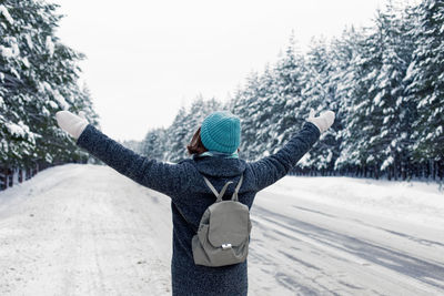 Girl in coat, with a backpack behind her back, stands on the side of the road, in a  winter forest