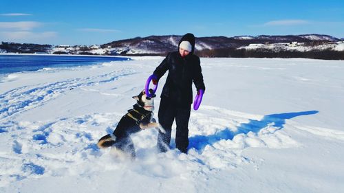 Woman playing with husky on deep snow against sky