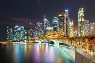 Illuminated bridge over river by buildings against sky at night