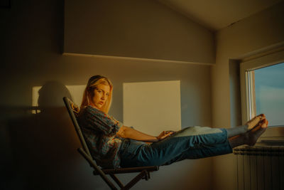 Side view of young woman sitting on chair at home