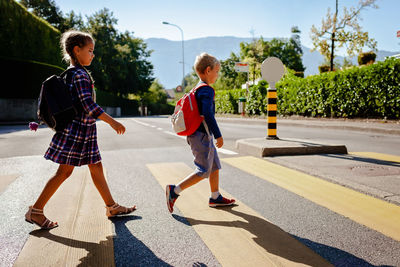 Kids with backpacks cross the road at crosswalk on the way to school. child safety, education