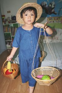 Cute boy carrying fruits in basket while standing on floor at home