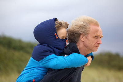 Man giving piggyback to grandson against sky