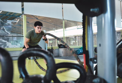 Focused asian man training with battle rope in a modern crossfit gym