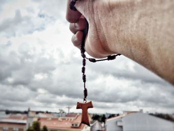 Close-up of hand holding cross against sky