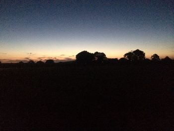 Silhouette trees on field against clear sky