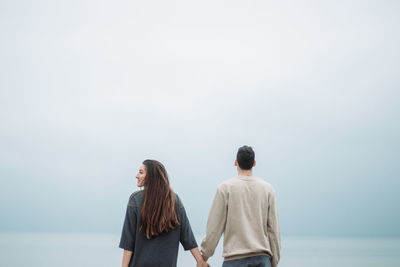 Rear view of people standing by sea against sky