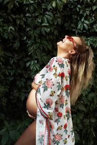 Side view of pregnant woman laughing while standing by plants