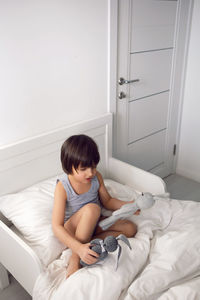 Child boy lies in a white children's bed with a blanket in a room with toys rabbits