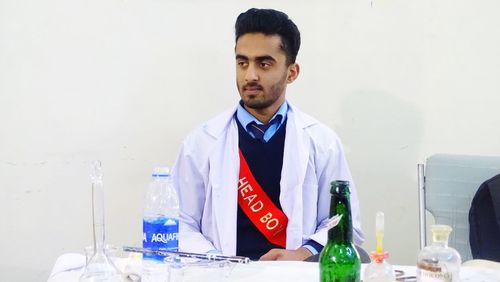 Young man standing by glass on table