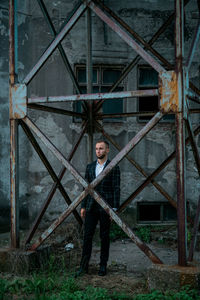 Young man looking away standing amidst metal structure