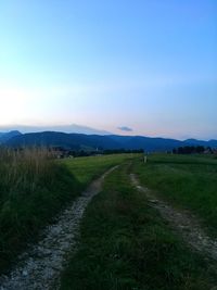 Empty road amidst field against sky