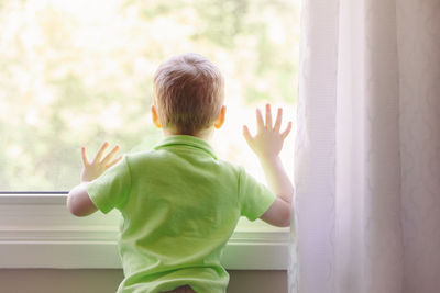 Rear view of boy looking through window