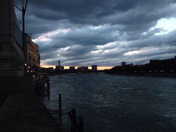 View of city at waterfront against cloudy sky