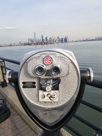 Close-up of coin-operated binoculars by cityscape against sky