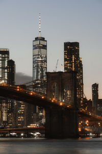 Low angle view of illuminated brooklyn bridge over river in city at dusk