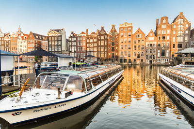 Sailboats moored on canal amidst buildings in city against sky