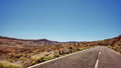Empty road along landscape against clear blue sky