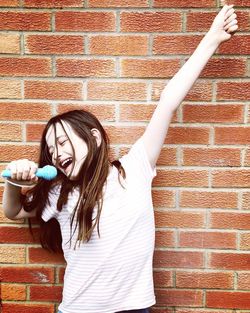Girl singing while standing against brick wall