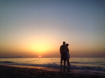 Silhouette friends standing on beach against clear sky during sunset