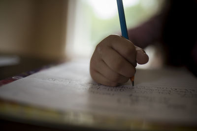 Cropped image of girl writing homework on table at home