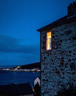 Illuminated building by sea against sky at night