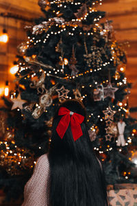 A brunette woman with a red bow in her hair sitting near a christmas tree with golden magic decor