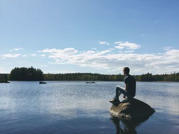 Man sitting on rock amidst lake against sky