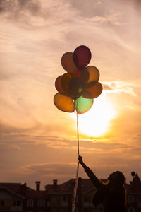 Low angle view of silhouette person holding balloons against sky during sunset