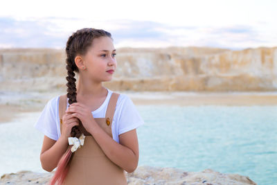 A pretty girl with long braid on the shore of the lake looks into the distance.