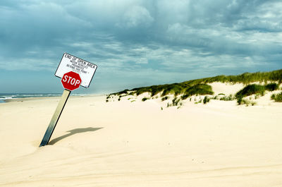 Stop sign at beach against cloudy sky