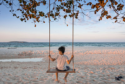 Rear view of woman sitting on beach against sky