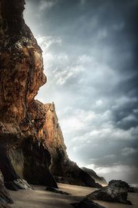 Low angle view of rock formation on shore against cloudy sky