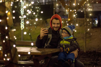 Father taking selfie with son while sitting at bench
