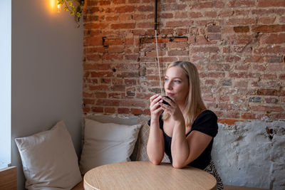Young woman using phone while sitting against wall
