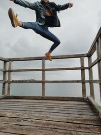 Low section of man jumping on pier against sea