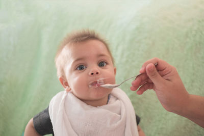 Hand feeding baby boy against wall at home