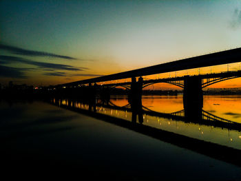 Silhouette bridge over river against sky at sunset